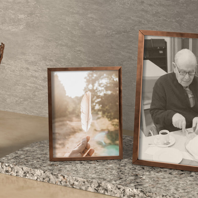 Kynttilä ja kaksi kuvakehystä, joista toisessa höyhen ja toisessa silmälasipäinen mies, joka leikkaa 90-vuotissyntymäpäiväkakkua.