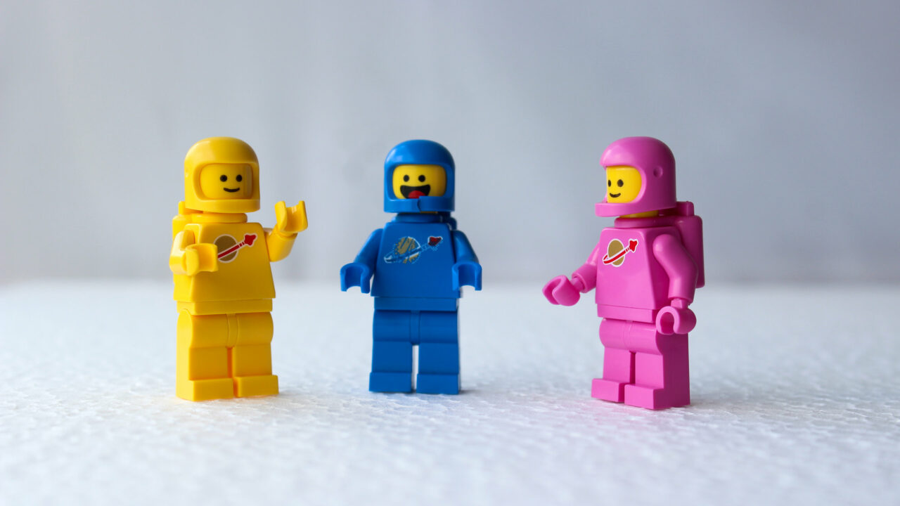 Kolme iloista, eri väristä lego-astronauttifiguuria seisoo vierekkäin.
