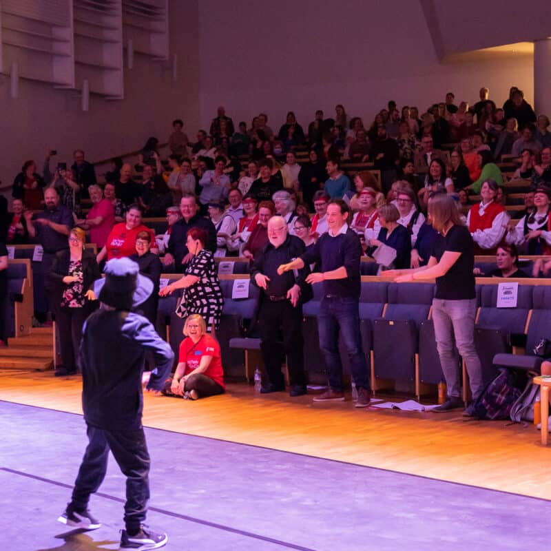 Kaksi lasta voimistelee lavalla ja vetää yleisönkin mukaan.