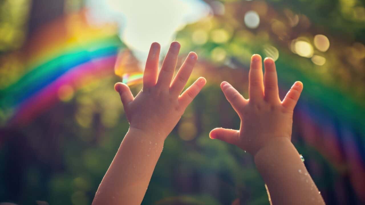 Lapsen kädet ilmassa. Taustalla metsää ja sateenkaari.